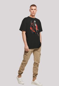Black t-shirt featuring a colorful graphic of a character with armor and a cape. Paired with beige cargo pants and white sneakers.