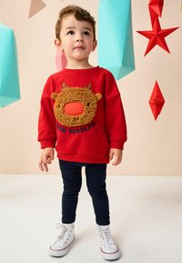 Czerwony sweter z teksturowanym wzorem renifera z rogami i nosem, w połączeniu z granatowymi leginsami i białymi trampkami.