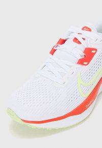 Bijele atletske tenisice s mrežastim gornjim dijelom, crvenim detaljima i potplatom u limeta zelenoj boji. Imaju vezice i istaknuti Swoosh logo sa strane.
