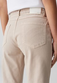 Lichtbeige jeans met een rechte snit, voorzien van twee achterzakken en subtiele stikseldetails. Gemaakt van denim met een gladde textuur.