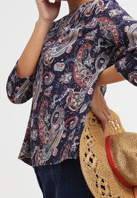 Marinblus med paisleymönster, tillverkad av lättviktsmaterial, har trekvartslånga ärmar och en avslappnad passform. Håller en halmhatt.