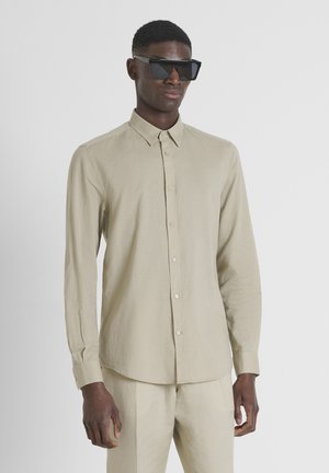 Camisa de manga larga beige con cuello abotonado, hecha de una tela ligera, que presenta una textura suave y pantalones beige a juego.