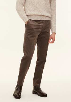 Bruine corduroy broek met verticale ribbels, slim fit, en voorzakken, met een gladde textuur, gecombineerd met een lichtgrijze trui en zwarte laarzen.