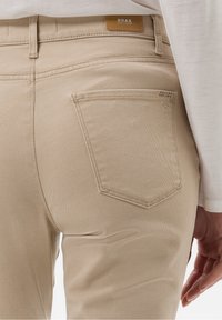 Pantalones de denim de algodón beige con un diseño ajustado, que cuentan con un bolsillo trasero y una pequeña etiqueta con logo en la cinturilla.