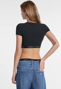 T-shirt nera cropped con maniche corte, dotata di fascia con logo. Abbinate a jeans blu a vita alta, con tasche e dettagli di cucitura.