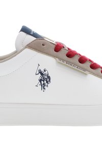 Witte sneaker met een gladde leren afwerking, rode veters, beige suède accenten en een blauwe tong. Heeft een zwarte polospeler grafiek aan de zijkant.
