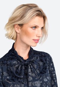 Navy blouse with a tie neck, featuring a textured pattern resembling animal print in dark tones, made of soft fabric.