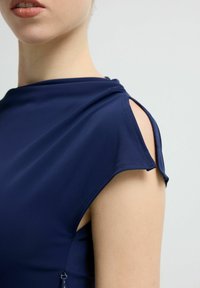 Granatowy top bez rękawów z okrągłym dekoltem, wycięciem na ramionach oraz gładką tkaniną wykończoną starannym przeszyciem wzdłuż krawędzi.