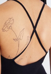 Μαύρη αμάνικη μπλούζα με σταυρωτές ράντες στην πλάτη, με λεία υφή και λουλουδένιο τατουάζ στον ώμο του φορέα.