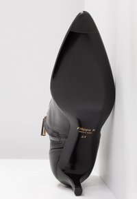 Chaussure noire en cuir à bout pointu avec un design élégant, dotée d'un petit talon kitten et de détails de couture subtils, étiquetée "Filippa K" à l'intérieur.