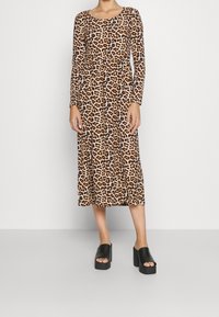 Vestido de leopardo con mangas largas, escote redondeado y falda fluida, combinado con sandalias de plataforma negras.