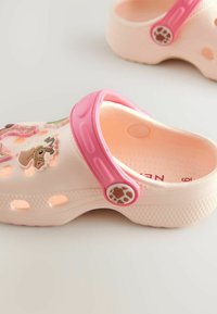 Rosa und cremefarbene Clogs mit dekorativen tierischen Pins, Belüftungsöffnungen zur Atmungsaktivität und einer strukturierten, rutschfesten Sohle.