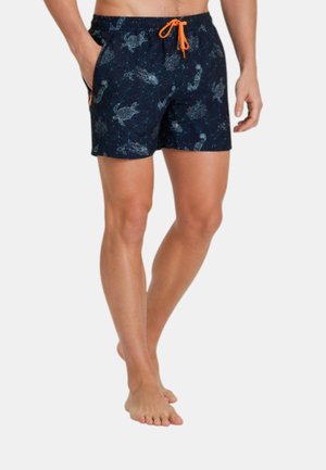 Torace e gambe maschili che indossano pantaloncini da bagno blu navy con motivi di tartaruga marina e cavalluccio marino, con coulisse arancione e tasche laterali.