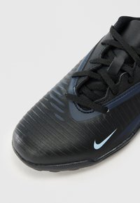 Chaussure de sport noire avec un dessus texturé, dotée d'un swoosh Nike bleu et de lacets, conçue pour la stabilité et la traction sur diverses surfaces.