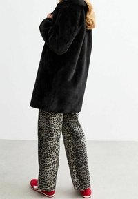 Černý kabát z umělé kožešiny s volným střihem, doplněný světle zbarvenými širokými kalhotami s leopardím potiskem a červenými botami. Hladká textura a ležérní design.