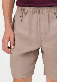 Pantalones cortos de algodón beige con cintura elástica, que cuentan con dos bolsillos frontales, costuras visibles y un ajuste relajado.