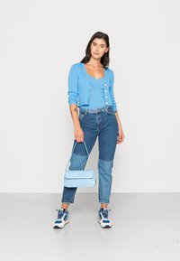 Lyseblå ribbestrikket cardigan med knapper, matchende tank topp, innvevde blå jeans og en liten blå veske; brukt med blå og hvite joggesko.