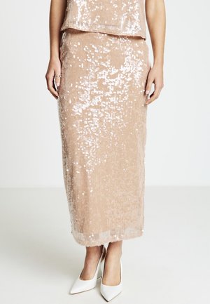 Sequined midi skirt in blush pink, featuring a fitted silhouette, shiny surface, and soft texture, paired with white pointed heels.