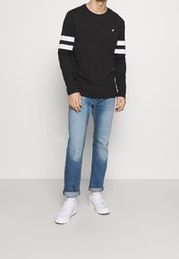 Svart långärmad skjorta med vita ränder på ärmarna, i kombination med ljusblå jeans och vita sneakers med rosa detaljer.