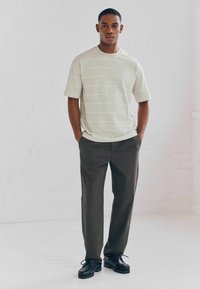 Light green short-sleeve t-shirt with horizontal white stripes, paired with dark green straight-leg trousers and black lace-up shoes.