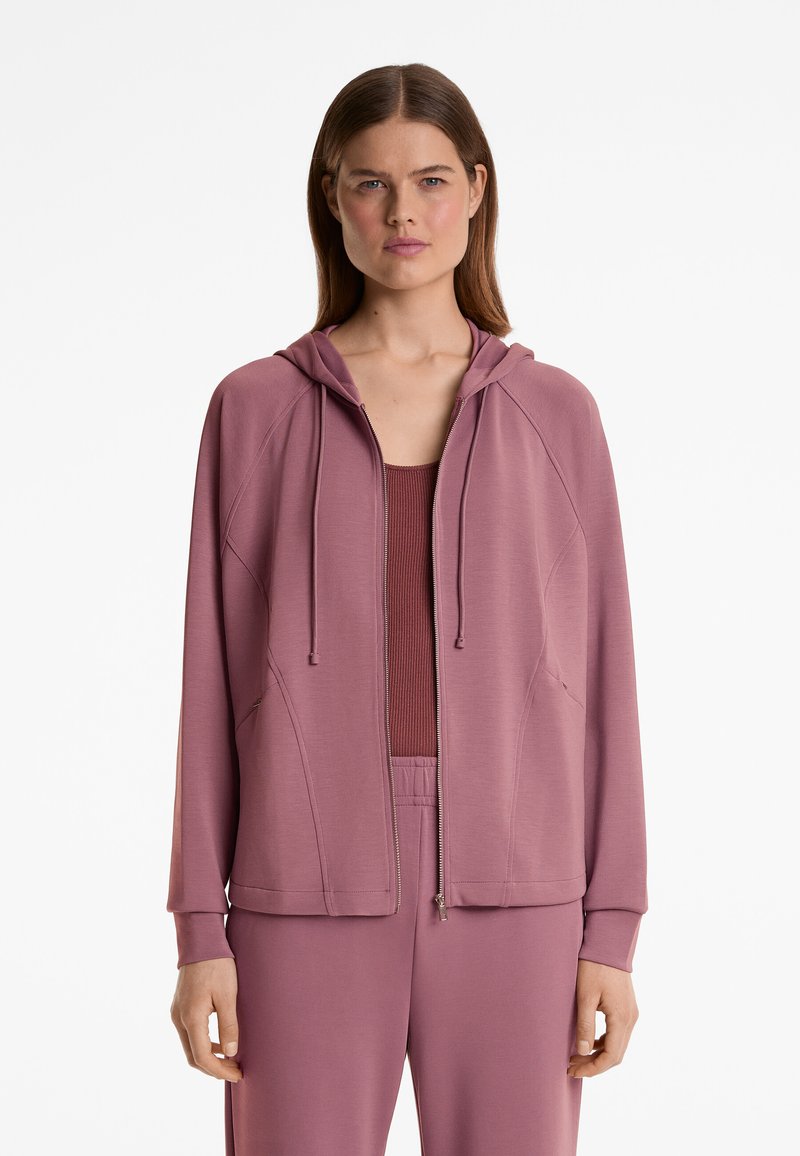 Helle lila Zip-Hoodie mit Kapuze, ausgestattet mit Raglanärmeln, Fronttaschen und strukturiertem Stoff. Getragen über einem passenden Oberteil.