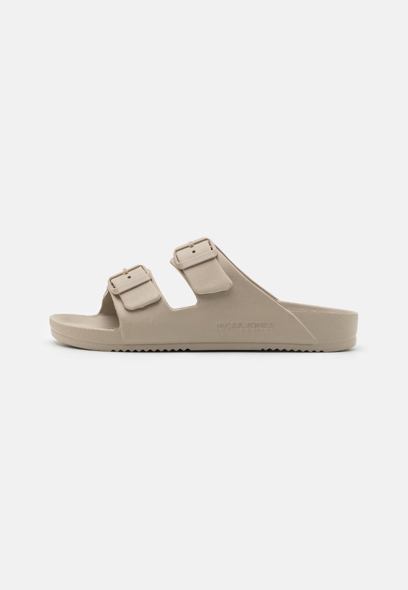 Beige slide sandalen met twee verstelbare gespen, open teen ontwerp, gestructureerde zool en merklogo aan de zijkant. Gemaakt van duurzaam materiaal.