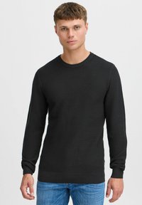 Svart strikkegenser med lange ermer, ribbestrikkede mansjetter og rund hals. Brukt sammen med blå jeans med strukturert overflate.