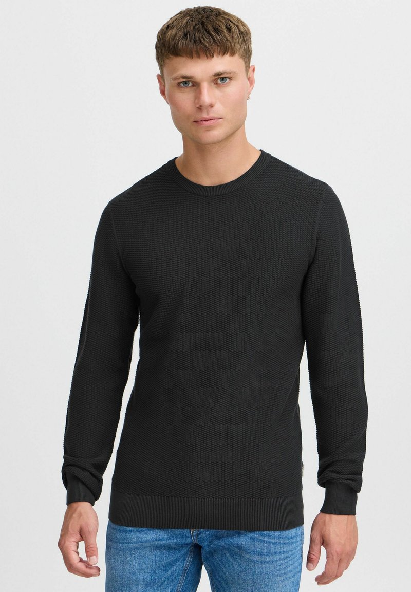 Svart strikkegenser med lange ermer, ribbestrikkede mansjetter og rund hals. Brukt sammen med blå jeans med strukturert overflate.