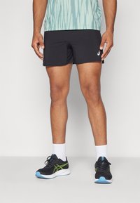 Black athletic shorts with a smooth texture, worn with white crew socks and black shoes accented with green and blue details.