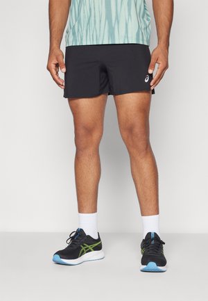 Pantalones cortos deportivos negros con una textura suave, usados con calcetines blancos y zapatos negros con detalles en verde y azul.