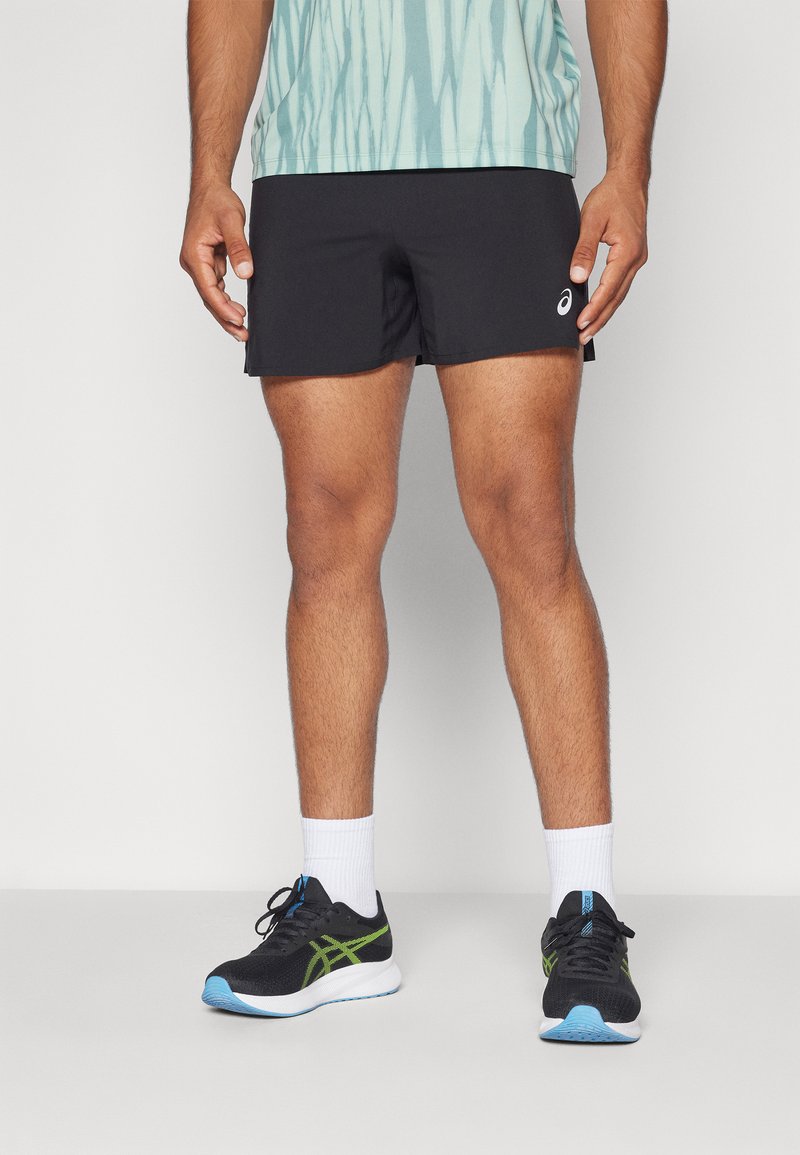 Black athletic shorts with a smooth texture, worn with white crew socks and black shoes accented with green and blue details.