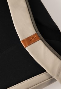 Borsa nera con una tracolla di colore crema con finitura texturizzata, arricchita da un'etichetta in pelle marrone stampata con "a/u."