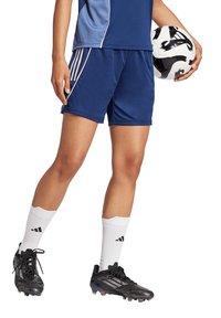 Blaue Sportshorts mit weißen Akzenten, kombiniert mit schwarzen Fußballschuhen und weißen Socken. Ein schwarz-weißer Fußball wird gehalten.