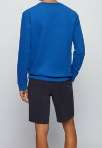 Blå sweatshirt med långa ärmar, rund halsringning och ribbade ärmslut. Matchas med mörkgrå shorts, som har två fickor och en enkel passform.