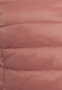 Bunda typu puffer v měkké růžové tkanině s horizontálně prošívanými sekcemi, viditelnými detaily šití a hladkým, lesklým povrchem.