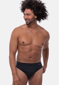 Zwarte gestreepte zwembroek met een zachte tailleband, getoond op een model in een staande positie tegen een plain witte achtergrond.