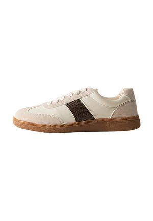 Zapatilla beige de caña baja con detalles en ante marrón claro, panel lateral texturizado oscuro, cordones blancos y suela de goma marrón.
