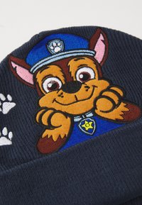 Mørkeblå strikket lue med brodert kartonhund karakter i politiform, med fremtredende ansiktstrekk og poteavtrykk detaljer.