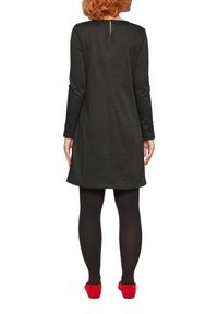 Schwarz-karierter Kleid mit langen Ärmeln, einem Schlitz hinten und einem lockeren Schnitt, kombiniert mit schwarzen Strumpfhosen und roten Schuhen.