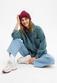Chemise en denim teal, avec deux poches devant et fermeture à boutons. Assortie à un pantalon en jean large bleu clair et des baskets blanches épaisses. Bonnet bordeaux.