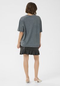 Tricou oversized gri, confecționat dintr-un material moale, cu mâneci scurte și guler rotund, asociat cu o fustă din piele neagră cu volane. Design minimalist.