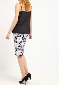 Top de satén negro sin mangas con tirantes ajustables, acompañado de una falda lápiz negra con flores a la altura de la rodilla. Zapatos de tacón altos negros completan el atuendo.