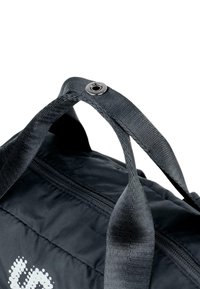 Bolsa de deporte negra con tejido texturizado, que presenta asas negras resistentes y un ojal plateado. Cierre de cremallera visible en el lateral.