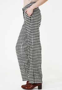 Pantalons à motif pied-de-poule en noir et blanc, avec une coupe décontractée, des poches latérales et une jambe légèrement évasée.