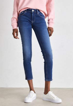 Vaqueros skinny de denim azul con cintura alta, de longitud cortada y dobladillo ligeramente deshilachado, combinados con zapatillas blancas.