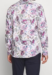 Camicia a maniche lunghe con base bianca, caratterizzata da un vivace motivo floreale in tonalità di rosa, verde e viola, realizzata in tessuto leggero.