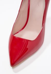 Chaussure à talon haut pointue en cuir verni rouge avec doublure intérieure beige, vue de dessus sur fond blanc.