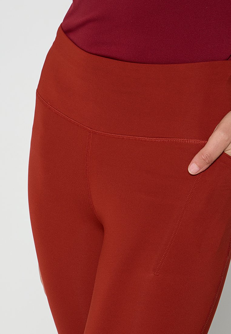 Leggings rossi a vita alta realizzati in materiale elasticizzato, con una texture liscia e una tasca laterale per comodità.