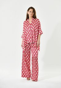 Röd och vit mönstrad, lättviktig klädsel med en löst sittande, kragskjorta med uppvikta ärmar och vida byxor.