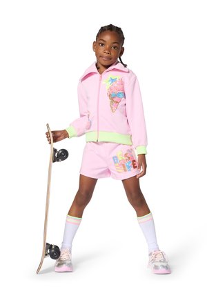 Tuta rosa con giacca corta con zip raffigurante un gelato e pantaloncini con la scritta "BEST LIFE" in glitter. Abbinata a uno skateboard.